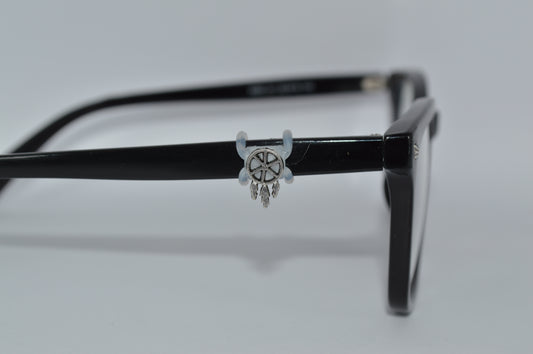 A silver dreamcatcher charm attached to the arm of a pair of black eyeglasses