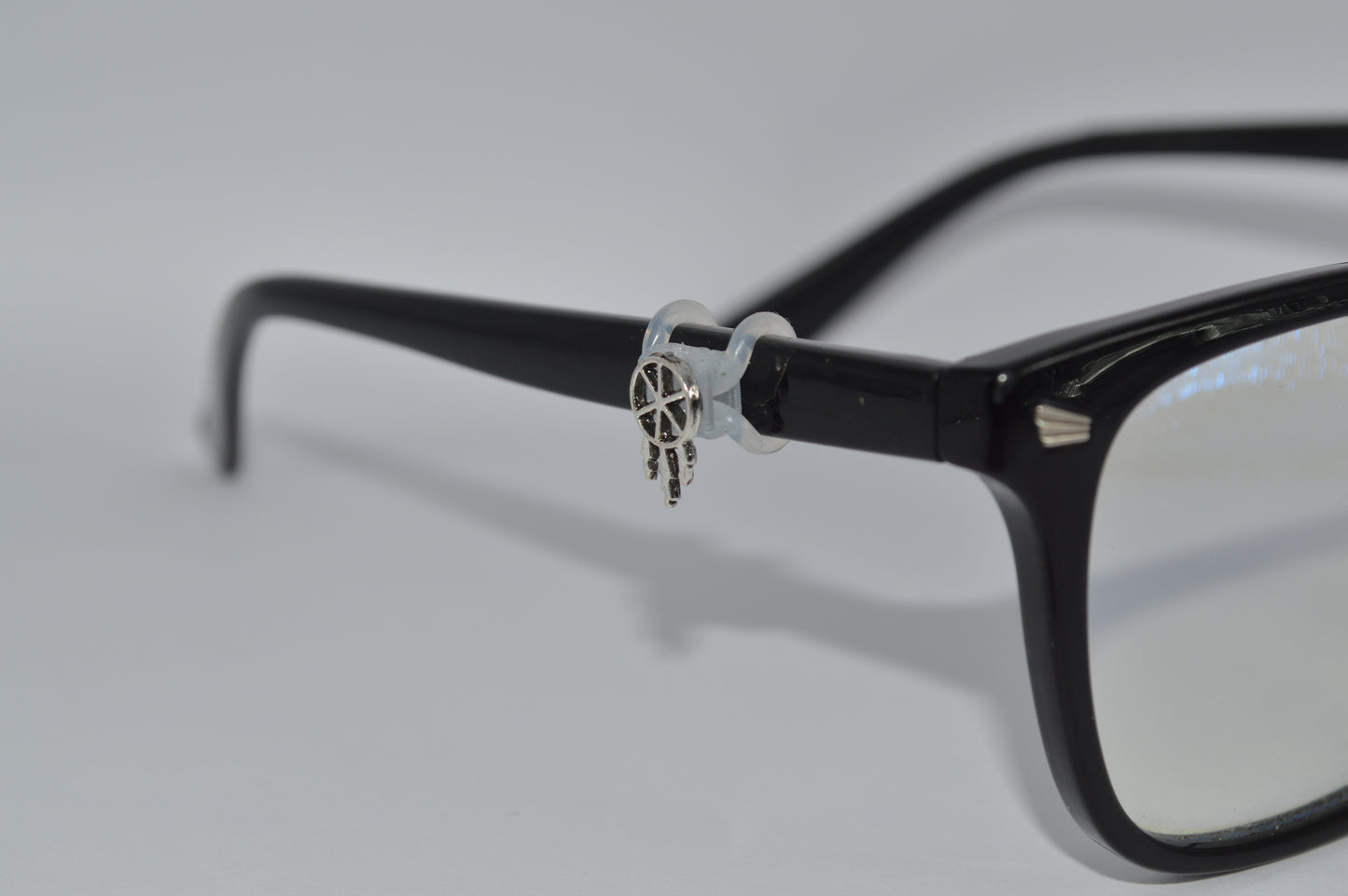 A silver dreamcatcher charm attached to the arm of a pair of black eyeglasses