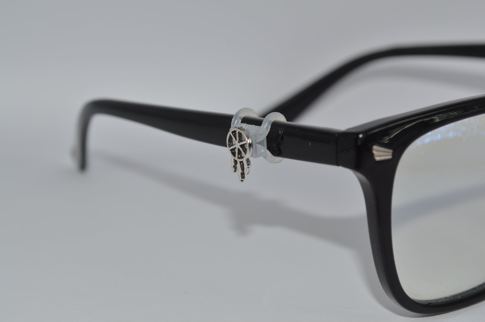 A silver dreamcatcher charm attached to the arm of a pair of black eyeglasses