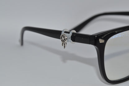 A silver dreamcatcher charm attached to the arm of a pair of black eyeglasses
